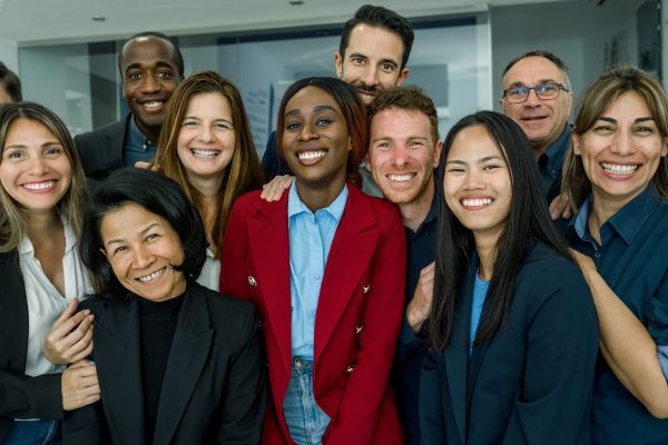Group of cheerful multiethnic people in formal clothes smiling and looking at camera while standing in modern office