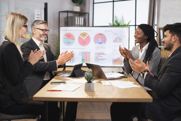 Business negotiations in office room. Team of attractive successful international corporate workers sitting at table while working together and applauding for successful business strategy of company